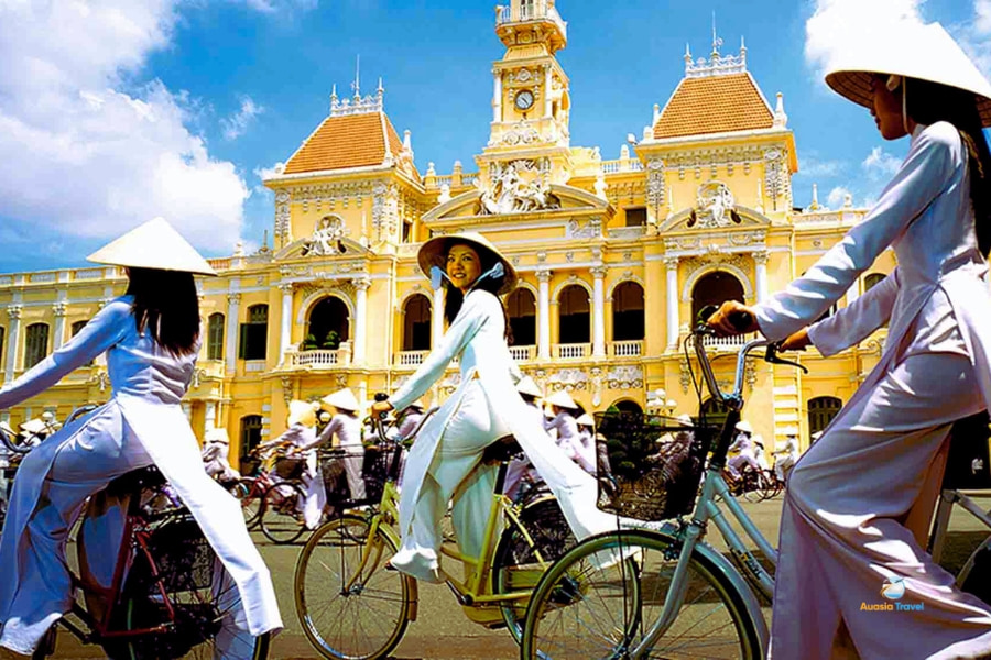 Vietnamese women wearing Ao Dai cycling past City Hall in Ho Chi Minh – Auasia Travel